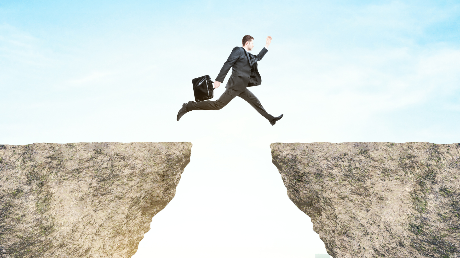 Man with a briefcase jumping over a small cliff