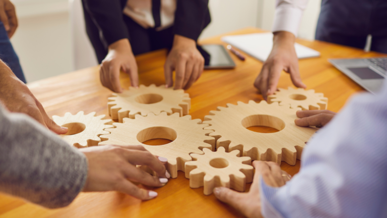 cropped image of office workers attaching wooden gears to each other on a desk in the office. Concept of effective business management, collaboration and team work